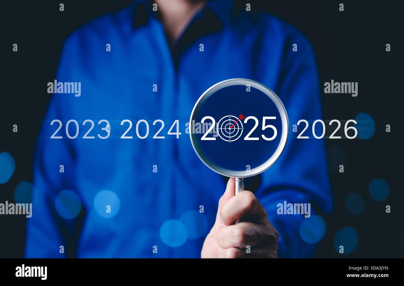 Concentrarsi sugli obiettivi aziendali del 2025 e sulla pianificazione futura. Una persona con una lente d'ingrandimento che evidenzia 2025 con un'icona di obiettivo, obiettivi futuri, strategia, Foto Stock
