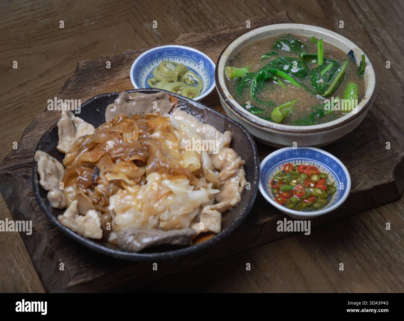 Gli ampi spaghetti di riso servono maiale marinato e cavolo cinese in una ricca salsa di sugo (Rad Na Moo). Il piatto è accompagnato da condimenti di fette di ch Foto Stock