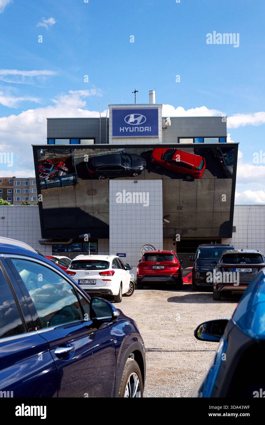 Logo dell'azienda Hyundai sull'edificio della concessionaria con auto e parti di ricambio che si riflettono in un contenitore di ferro il 29 maggio 2025 a Praga, repubblica Ceca. Foto Stock