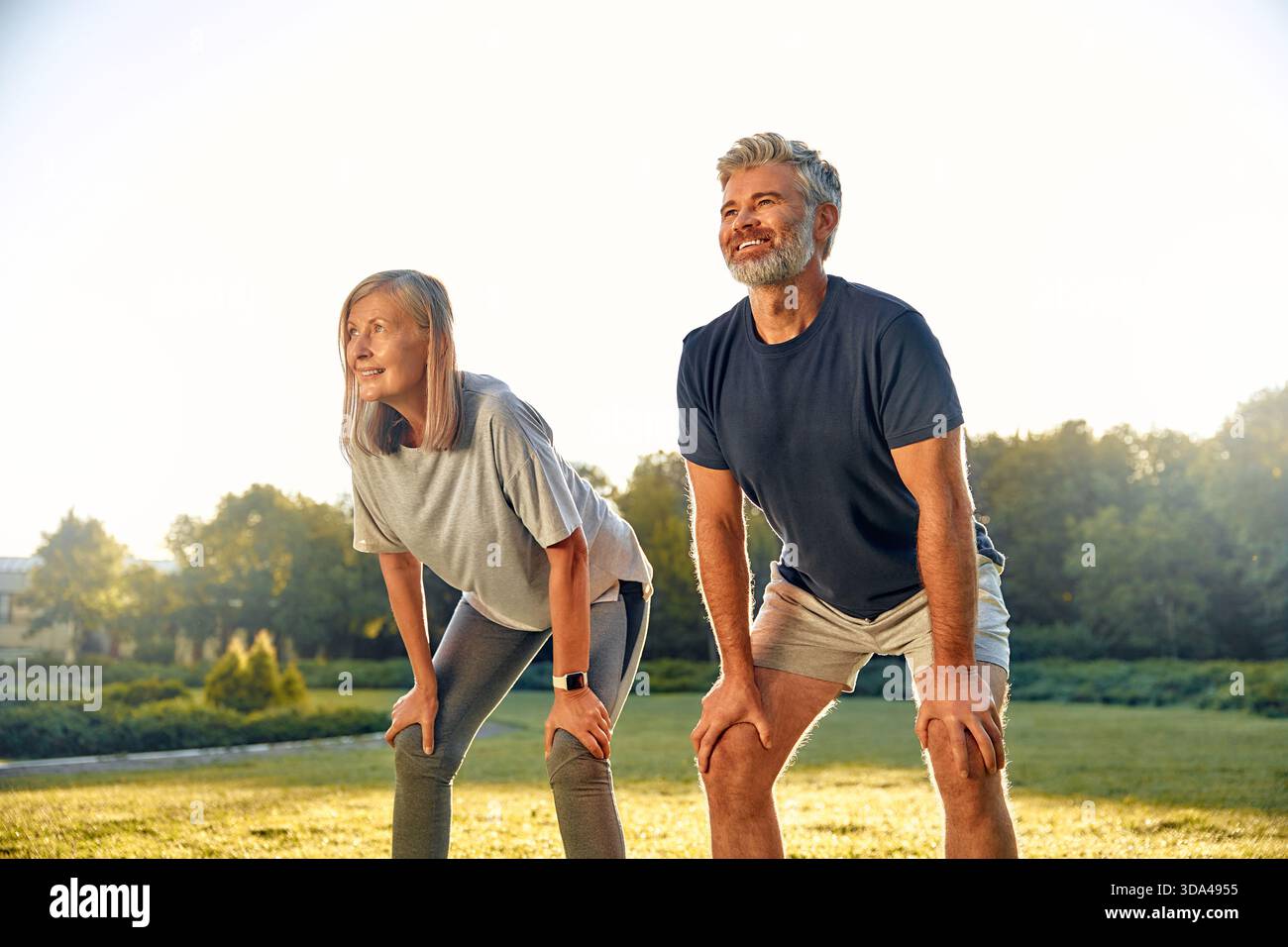 Una coppia gioiosa si allunga all'aperto in un parco tranquillo al tramonto, promuovendo fitness e benessere e godendosi la compagnia reciproca Foto Stock