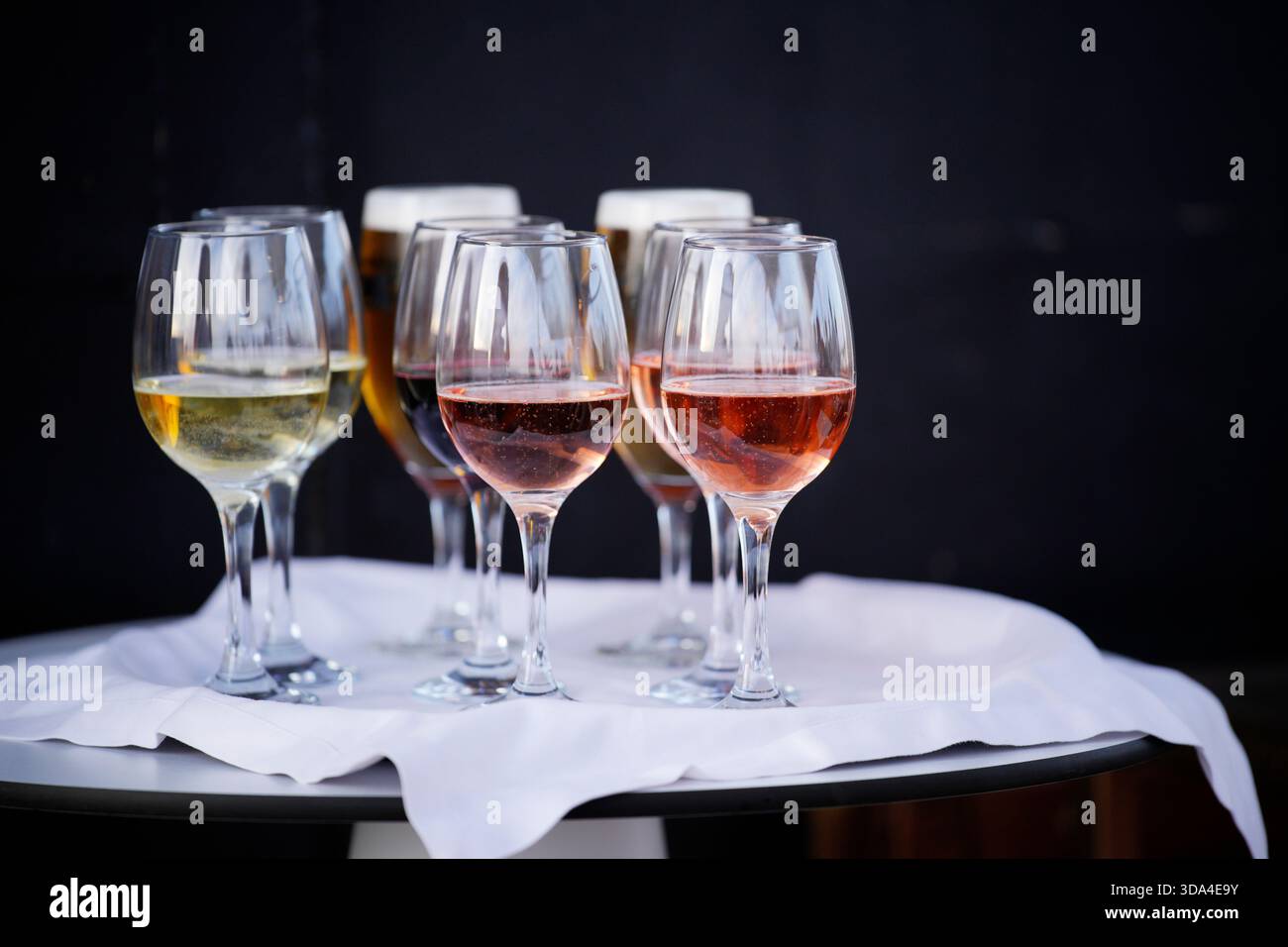 I bicchieri da vino contenenti diversi tipi di vino, tra cui bianco, rosato ed eventualmente rosso, sono disposti su un tavolo con una tovaglia bianca, pronti per un Foto Stock