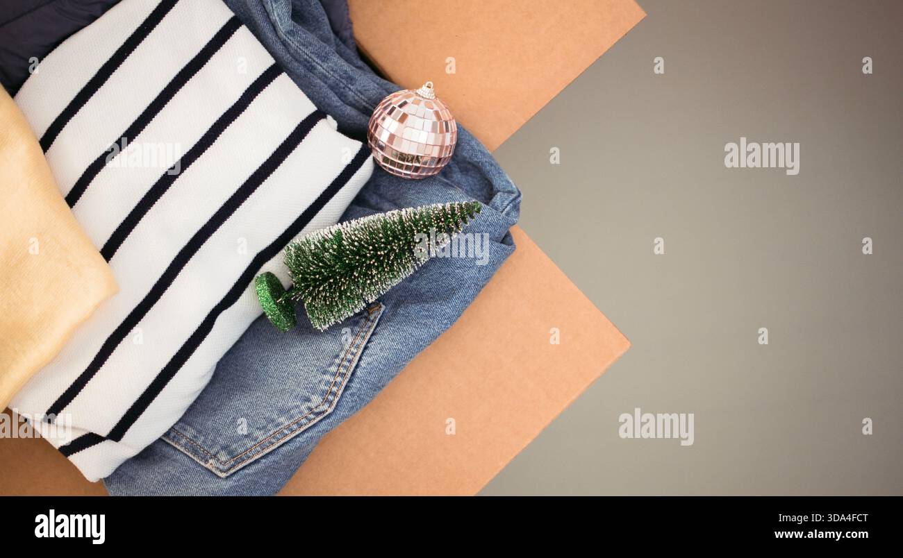 Scatola di donazioni natalizie per beneficenza con mini albero di Natale e bauble decorativo. Scatola di cartone piena di caldi abiti invernali. Vista dall'alto Foto Stock