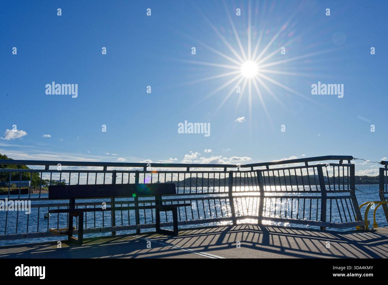 Il ponte e la panchina catturano la luce calda mentre il sole svanisce e lancia raggi morbidi in ogni direzione attraverso l'acqua pallida, l'aria calma e i riflessi luminosi Foto Stock