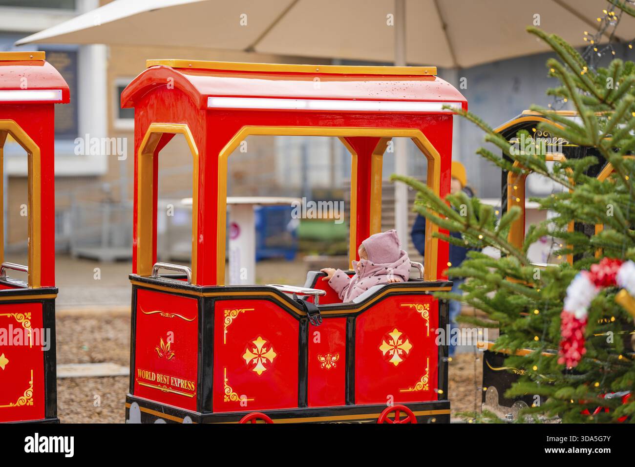 Un bambino siede su un treno rosso in miniatura accanto a un albero di Natale in un mercato, Sindelfingen, quartiere di Boeblingen, Germania Foto Stock