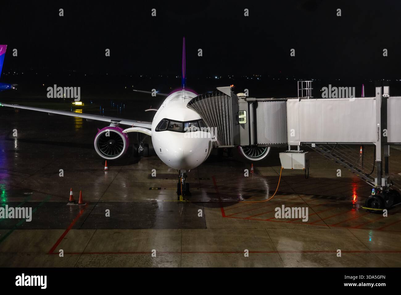 Bari, Italia, 28 novembre 2025. l'aereo wizz air si imbarca di notte su un asfalto bagnato tramite un ponte jet in un ambiente aeroportuale tranquillo, che mette in mostra i viaggi aerei Foto Stock