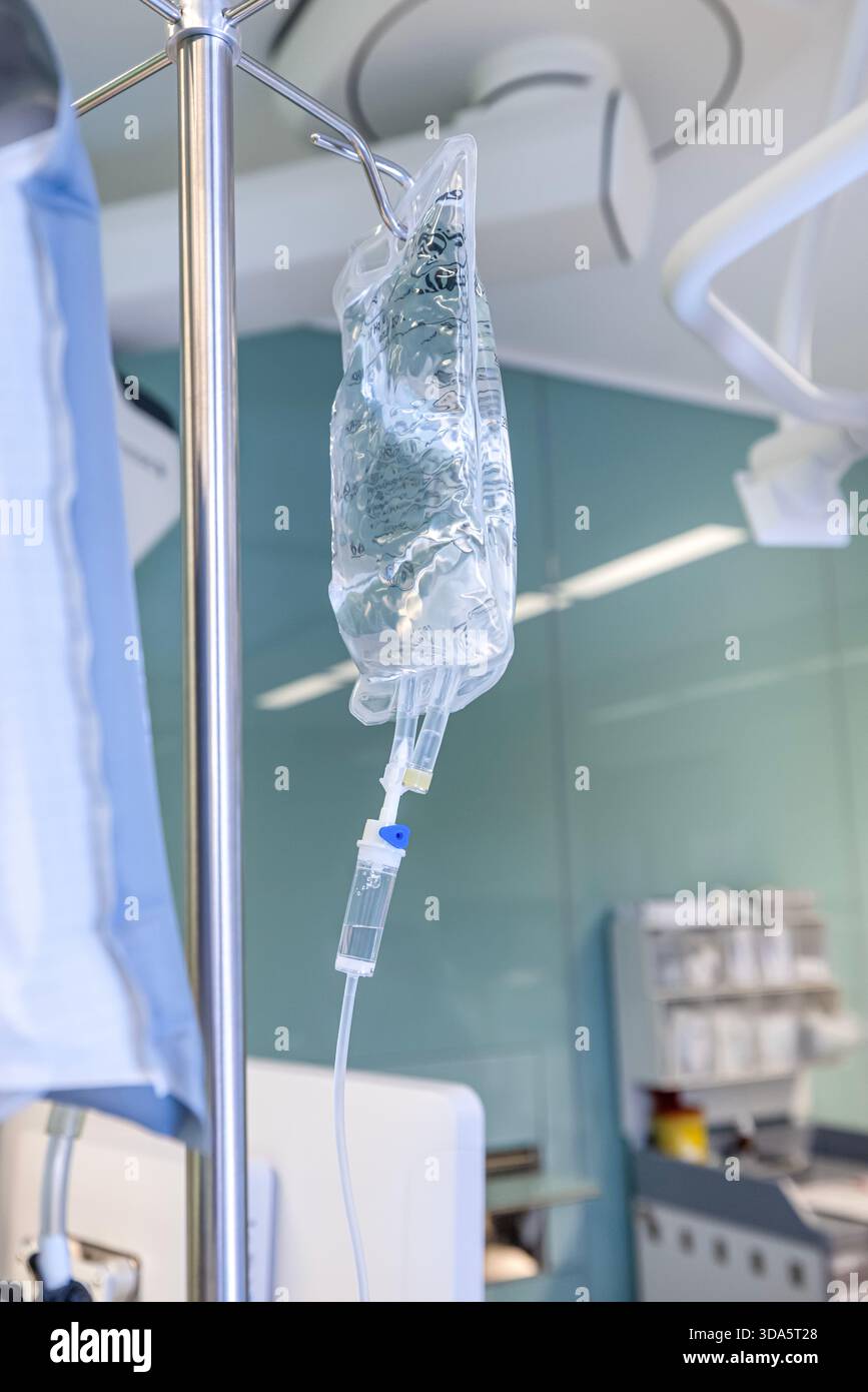 Infusione endovenosa in primo piano somministrata a un paziente durante l'intervento chirurgico in una sala operatoria sterile, che mostra le apparecchiature mediche e la cura intraoperatoria del paziente. Foto Stock