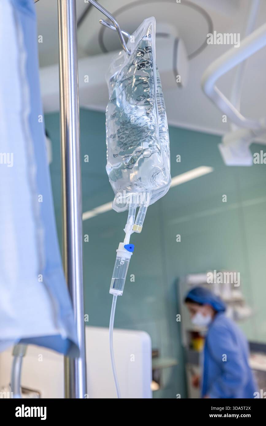 Infusione endovenosa in primo piano somministrata a un paziente durante l'intervento chirurgico in una sala operatoria sterile, che mostra le apparecchiature mediche e la cura intraoperatoria del paziente. Foto Stock