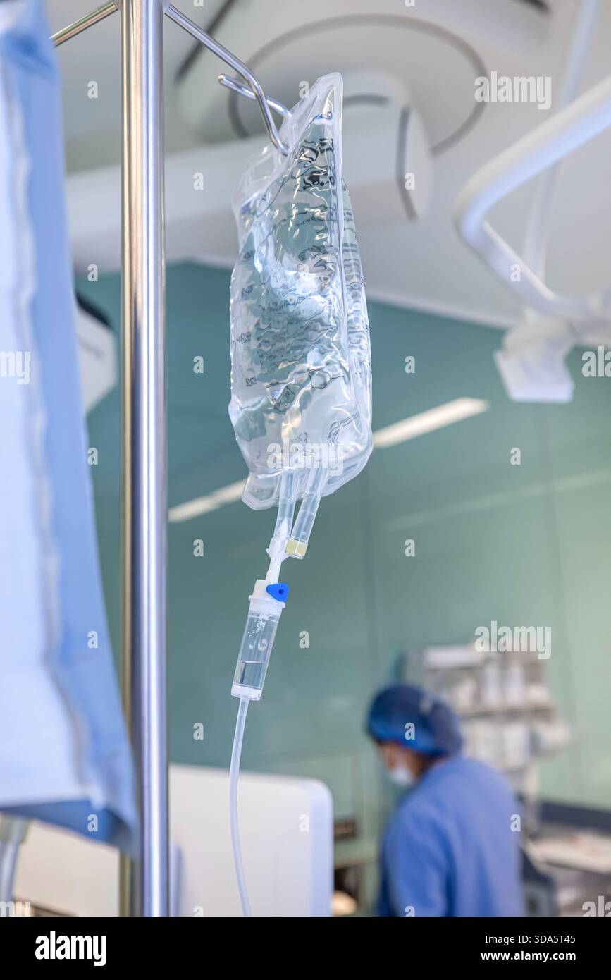 Infusione endovenosa in primo piano somministrata a un paziente durante l'intervento chirurgico in una sala operatoria sterile, che mostra le apparecchiature mediche e la cura intraoperatoria del paziente. Foto Stock