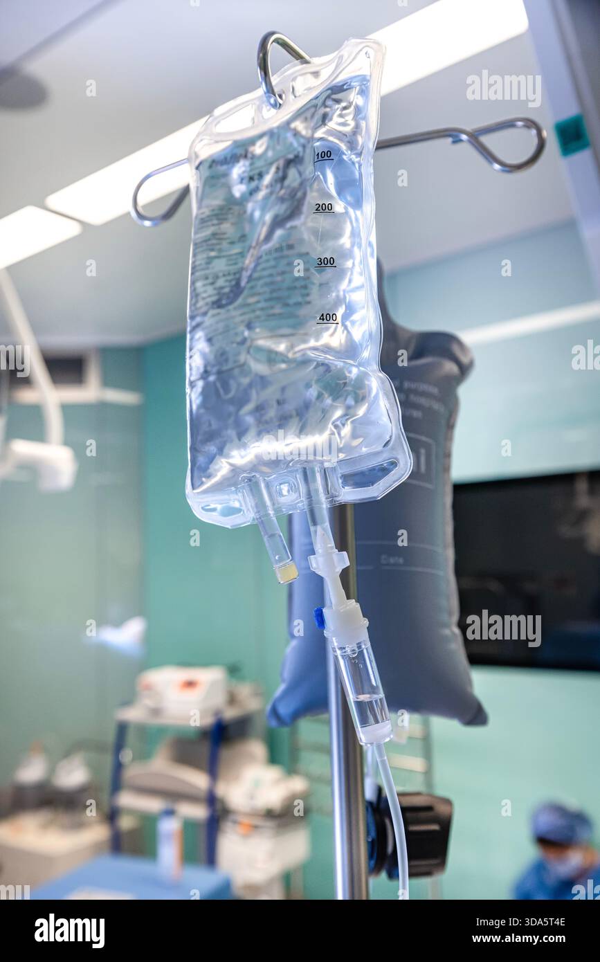 Infusione endovenosa in primo piano somministrata a un paziente durante l'intervento chirurgico in una sala operatoria sterile, che mostra le apparecchiature mediche e la cura intraoperatoria del paziente. Foto Stock