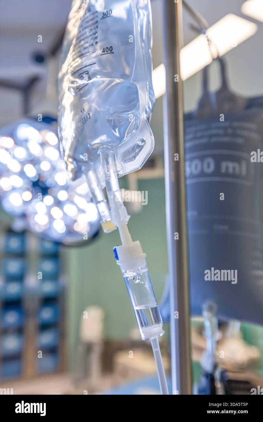 Infusione endovenosa in primo piano somministrata a un paziente durante l'intervento chirurgico in una sala operatoria sterile, che mostra le apparecchiature mediche e la cura intraoperatoria del paziente. Foto Stock