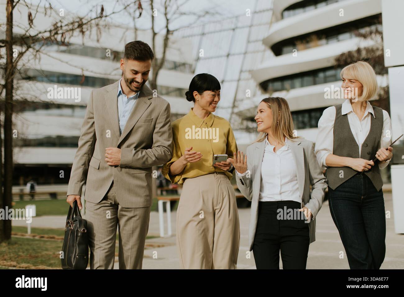 Quattro professionisti passeggiano insieme in una vivace zona d'affari, conversando e godendosi il bel tempo. Il loro abbigliamento riflette un mod Foto Stock