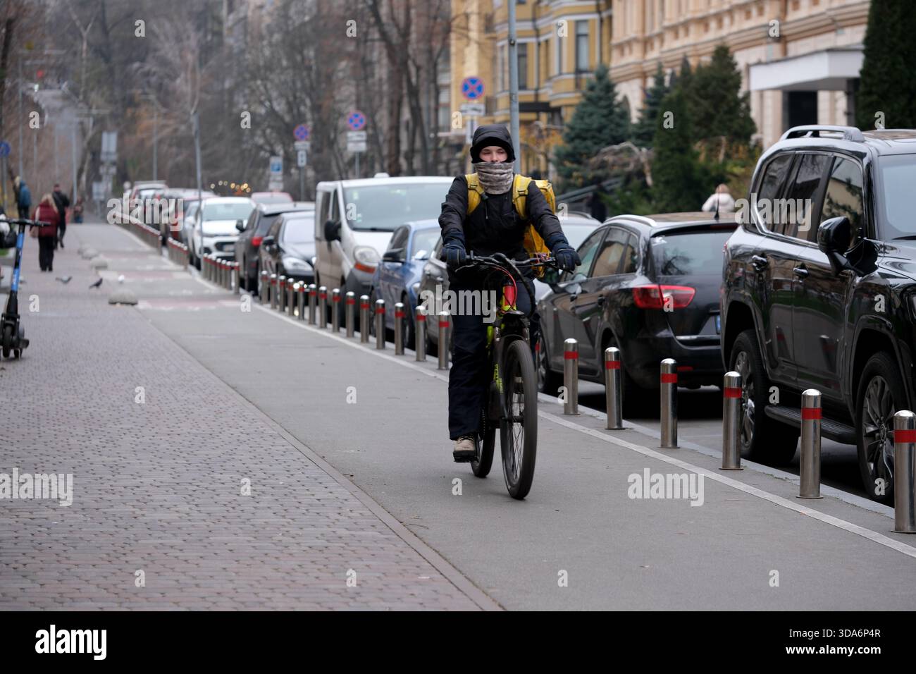 Un motociclista attento con abiti caldi percorre una strada trafficata costeggiata da auto parcheggiate. Kiev, Ucraina. 8 dicembre 2025. Foto Stock