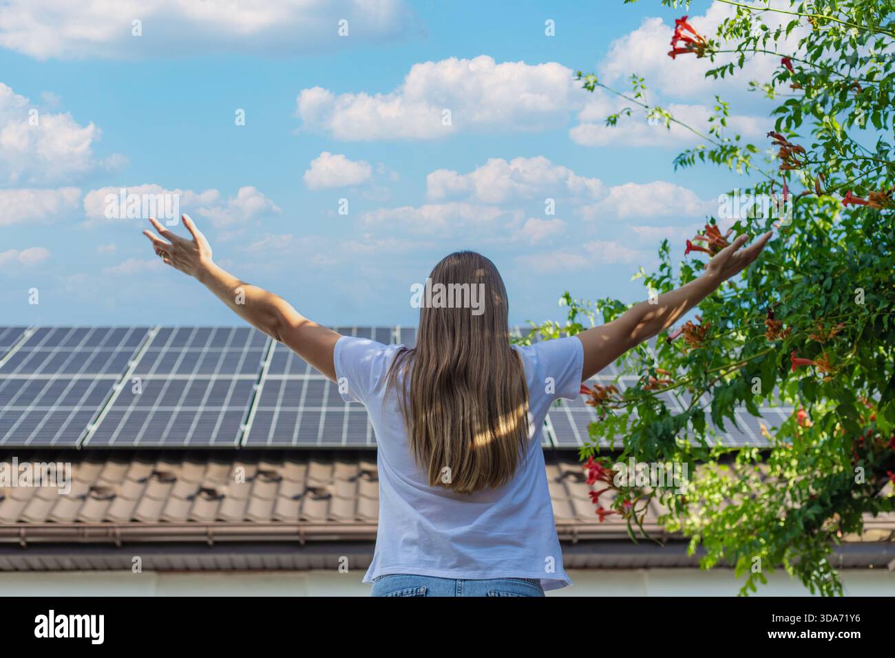 Donna con le braccia alzate di fronte a una casa con pannelli solari e tromba in fiore. Foto Stock