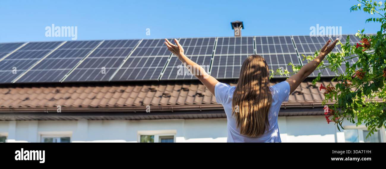 Donna con le braccia alzate di fronte a una casa con pannelli solari e tromba in fiore. Foto Stock