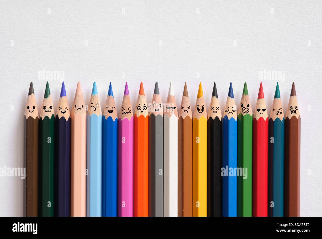 Linea di matite colorate che mostrano varie emozioni disegnate sui loro suggerimenti, rappresentando diversità e sentimenti collettivi Foto Stock