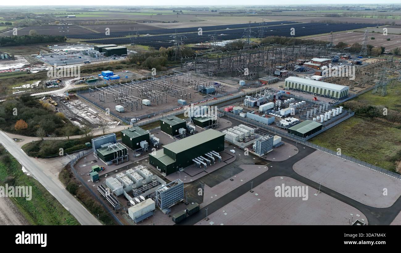 Veduta aerea di un moderno paesaggio industriale con un complesso di edifici e infrastrutture elettriche in contrasto con i campi arabili pianeggianti, su Foto Stock