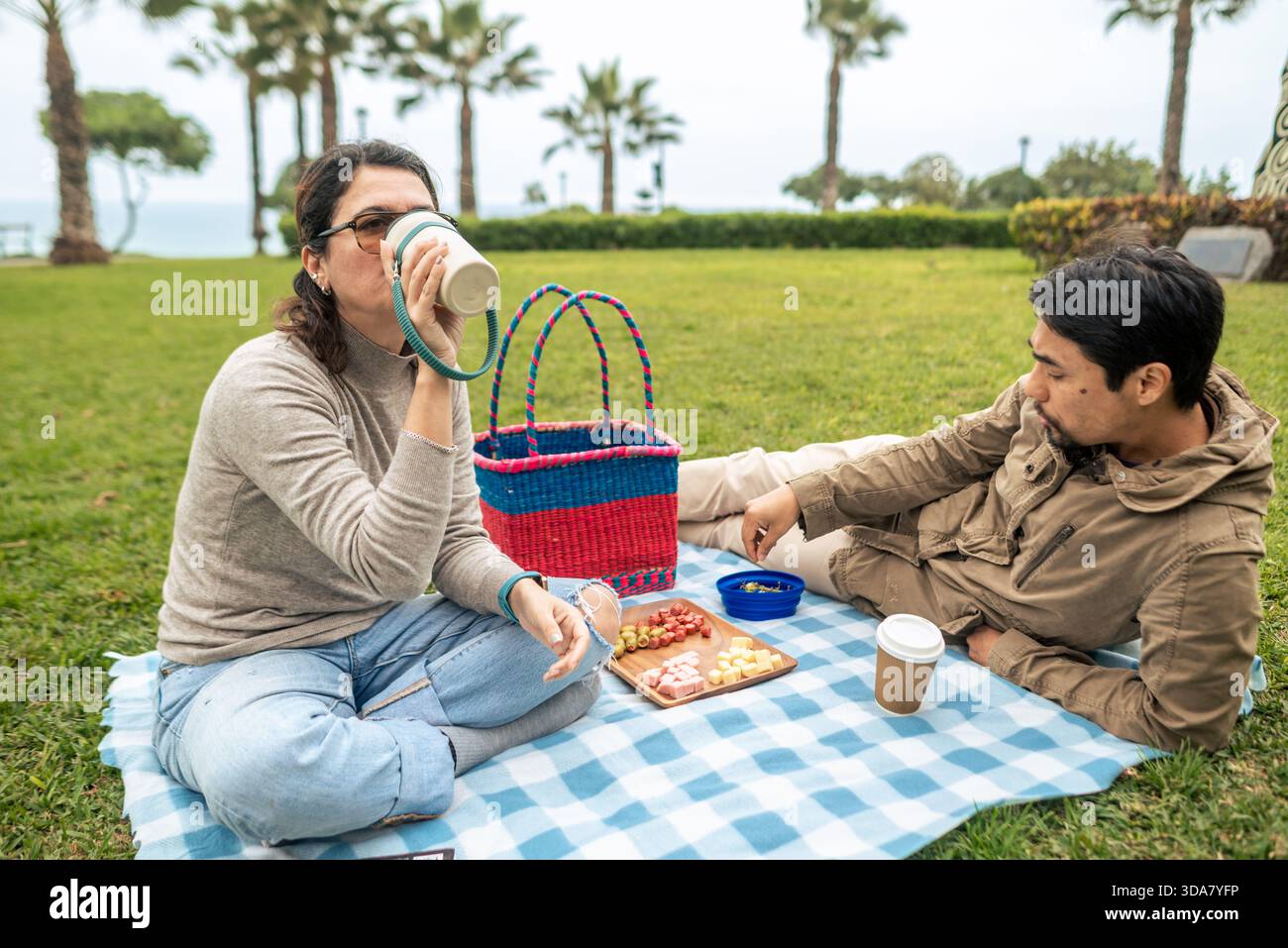 Una donna beve dalla sua bottiglia mentre il suo partner ama mangiare durante un picnic nel parco Foto Stock