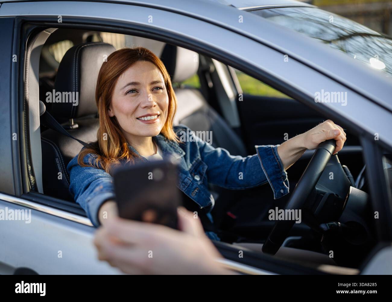 Una donna siede in macchina sorridendo mentre si prepara a pagare al drive-thru. La scena mostra un pomeriggio impegnativo in un fast food. Foto Stock