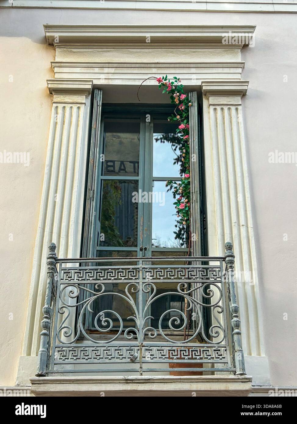 Incantevole balcone vintage con ringhiera in ferro ornata, alte finestre con persiane e fiori rosa che si arrampicano su una facciata architettonica classica. - Immagine stock catturata con smartphone
