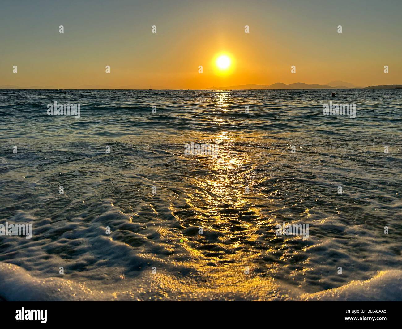 Il sole tramonta sulle calme onde dell'oceano, illuminando il cielo e l'acqua con ricche sfumature dorate e ambrate. - Immagine stock catturata con smartphone