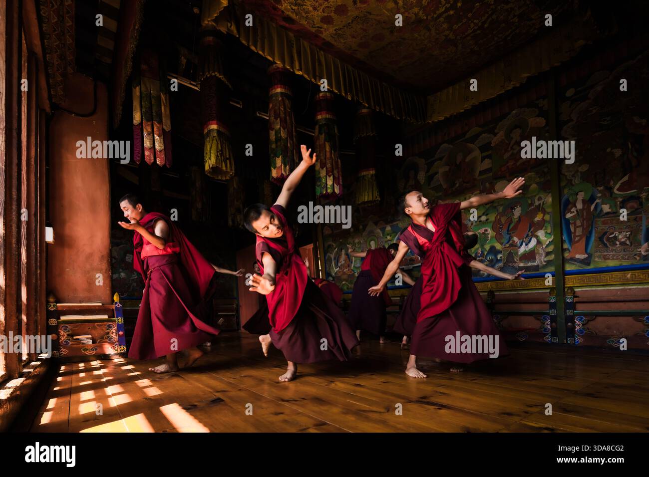 Jakar, Bhutan - 24 settembre 2025: Veduta dei monaci in vivaci vesti rosse danzano graziosamente in una stanza adornata da intricati murales e soffici gigli filtrati Foto Stock