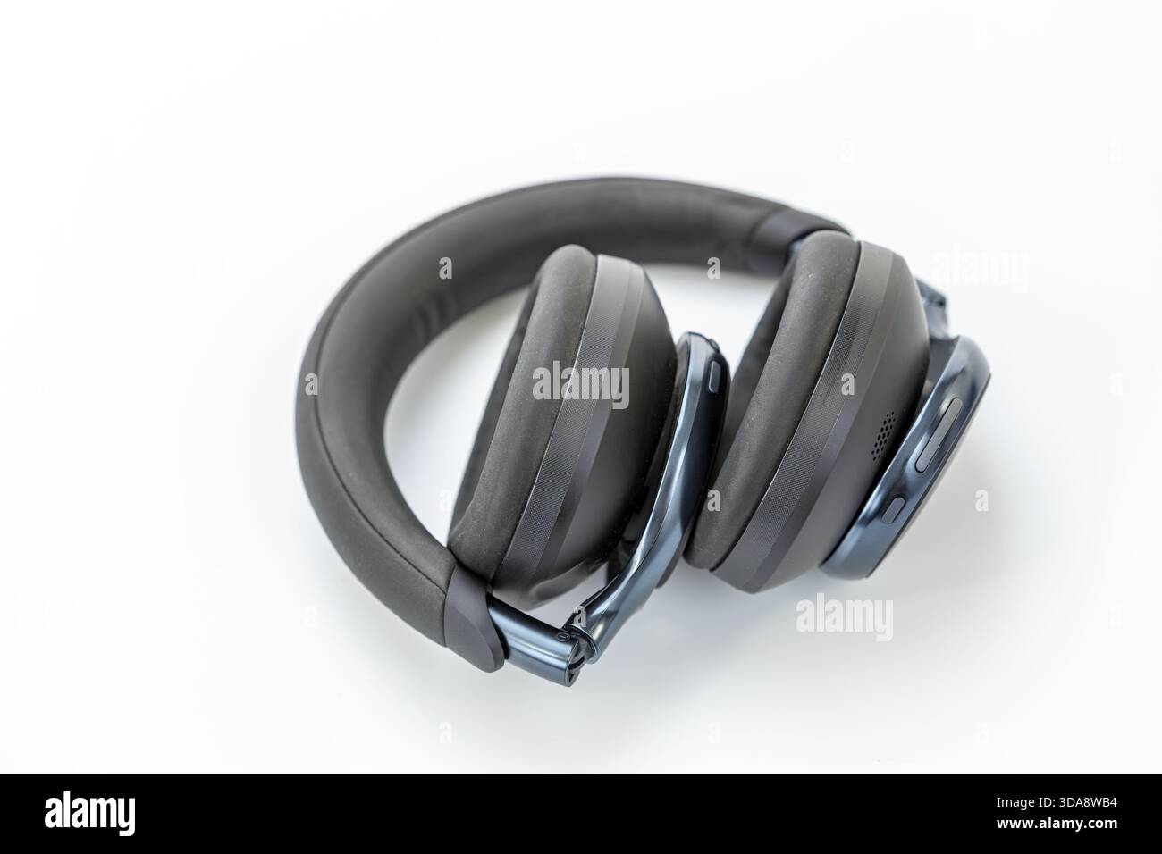 Un paio di cuffie auricolari wireless nere sono piegate su una superficie bianca, dotate di cuscinetti imbottiti, archetto imbottito e controllo visibile Foto Stock