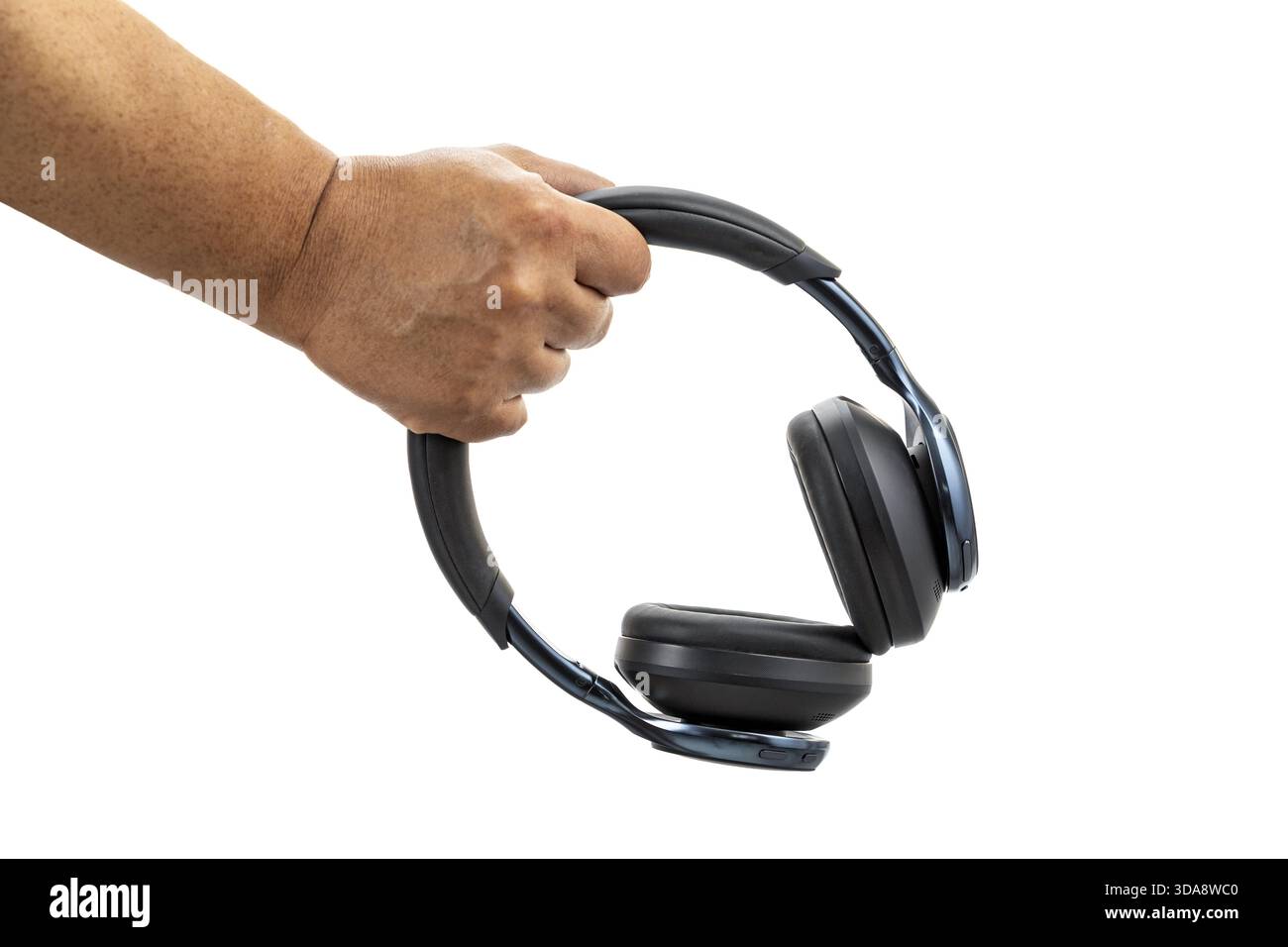 La mano di una persona regge un paio di cuffie auricolari wireless nere su un semplice sfondo bianco, mostrando le cuffie lateralmente e emp Foto Stock