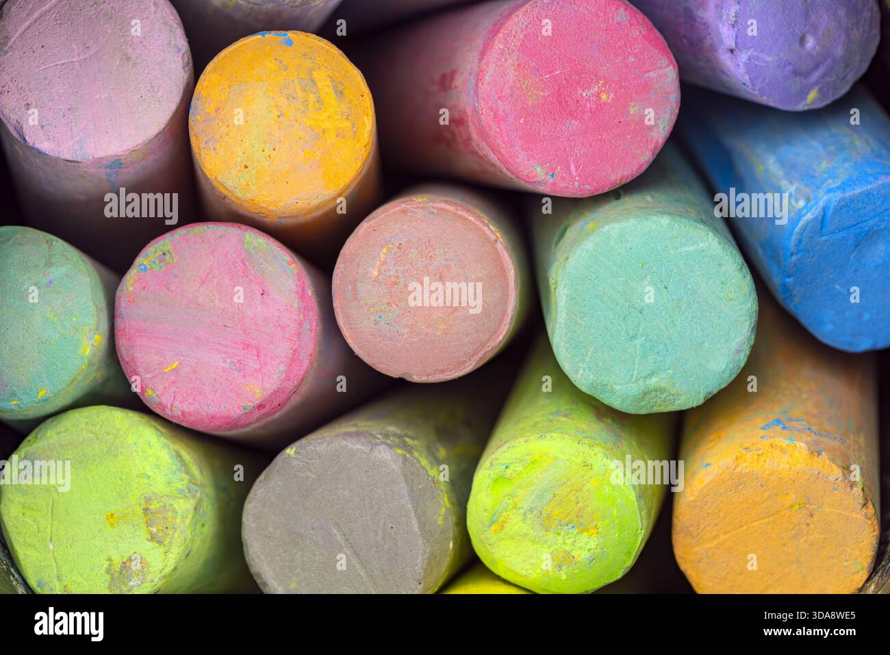 Una vista ravvicinata di diversi bastoncini colorati di gesso disposti in modo stretto insieme, mostrando vivaci sfumature di giallo, rosa, verde, blu, viola, e arancione Foto Stock