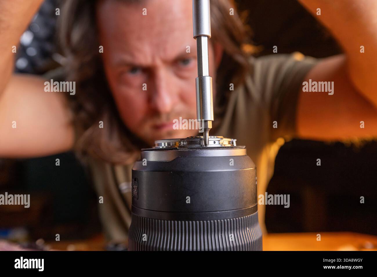 primo piano di un cacciavite che allenta le viti sull'elemento posteriore dell'obiettivo di una fotocamera e di un uomo concentrato sull'attività. Foto Stock