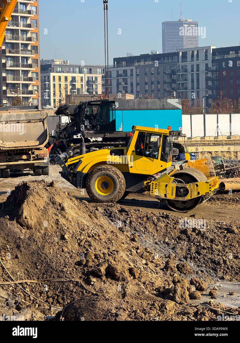 Rullo giallo per terreno in cantiere con edifici alti sullo sfondo. Sviluppo urbano, macchinari stradali, miglioramento delle infrastrutture e. Foto Stock