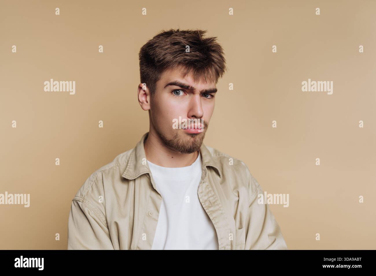 Giovane con un'espressione scettica su sfondo beige. Foto Stock