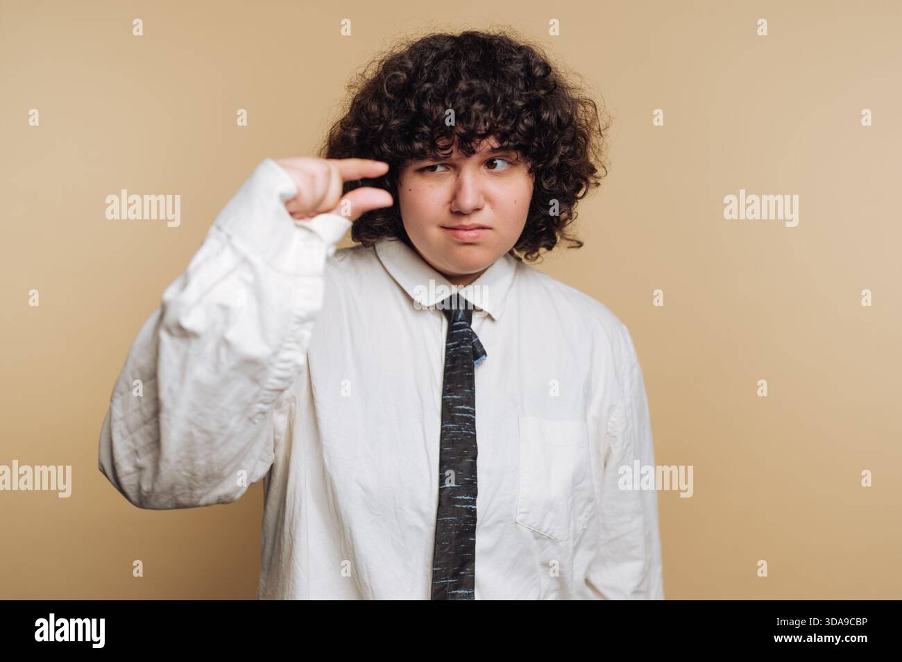 Una persona è al chiuso e indossa una maglietta e una cravatta grandi, mostrando un gesto con le dita per rappresentare qualcosa di piccolo. Lo sfondo è di colore semplice, Foto Stock