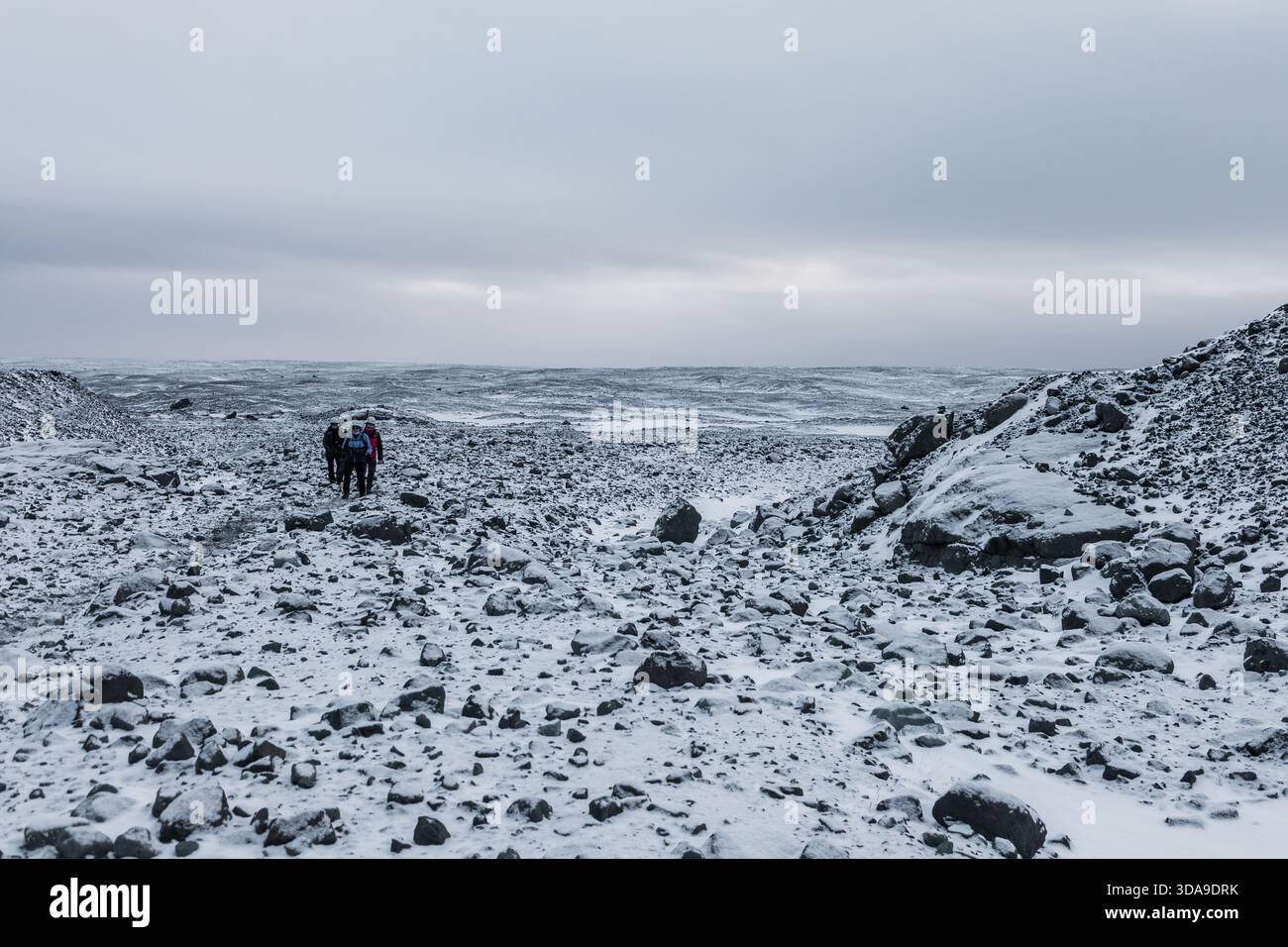 Islanda, 2 febbraio 2022 — Un gruppo di escursionisti attraversa una valle rocciosa e innevata in avvicinamento alla Grotta di ghiaccio blu vicino a Vatnajokull Foto Stock