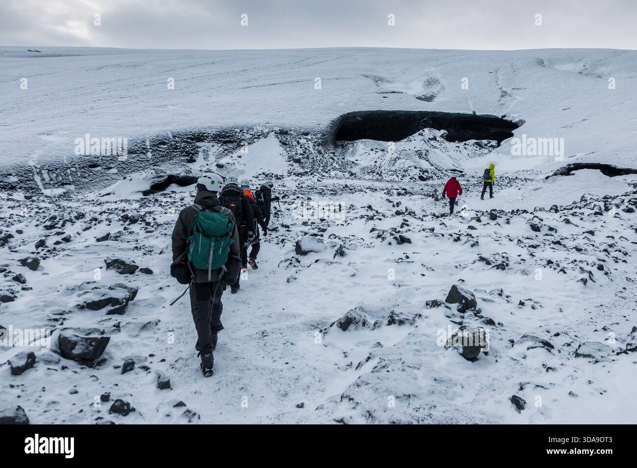 Islanda, 2 febbraio 2022 — Un gruppo di escursionisti attraversa una valle rocciosa e innevata in avvicinamento alla Grotta di ghiaccio blu vicino a Vatnajokull Foto Stock
