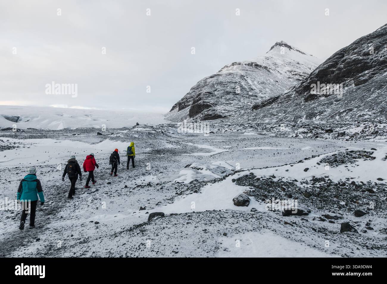 Islanda, 2 febbraio 2022 — Un gruppo di escursionisti attraversa una valle rocciosa e innevata in avvicinamento alla Grotta di ghiaccio blu vicino a Vatnajokull Foto Stock