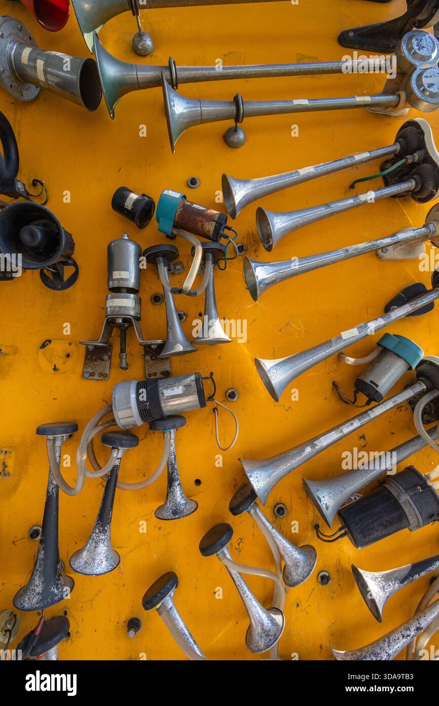 Vista ravvicinata degli avvisatori acustici pneumatici cromati e dell'attrezzatura da officina assortita montata su un pannello giallo brillante, evidenziando le apparecchiature audio industriali e la meccanica Foto Stock