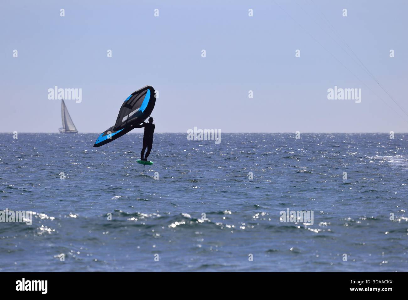 Cabedelo, Viana do Castelo, Portogallo - 7 maggio 2024: Windsurfer a bordo di una barca a vela blu sulle acque calme dell'oceano con una barca a vela sullo sfondo lontano Foto Stock