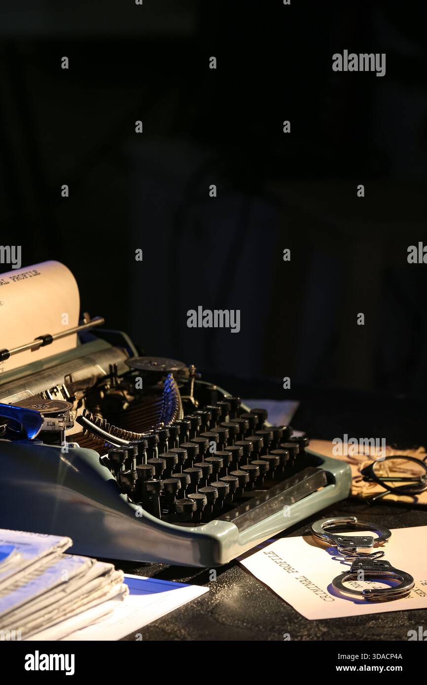 Macchina da scrivere retrò, manette e file criminali su un tavolo scuro Foto Stock
