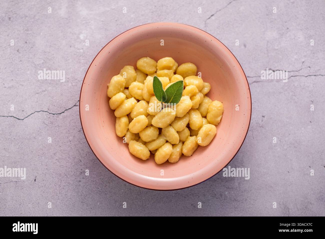Gnocchi con burro e foglie di salvia fresche serviti in una ciotola rosa su sfondo grigio Foto Stock