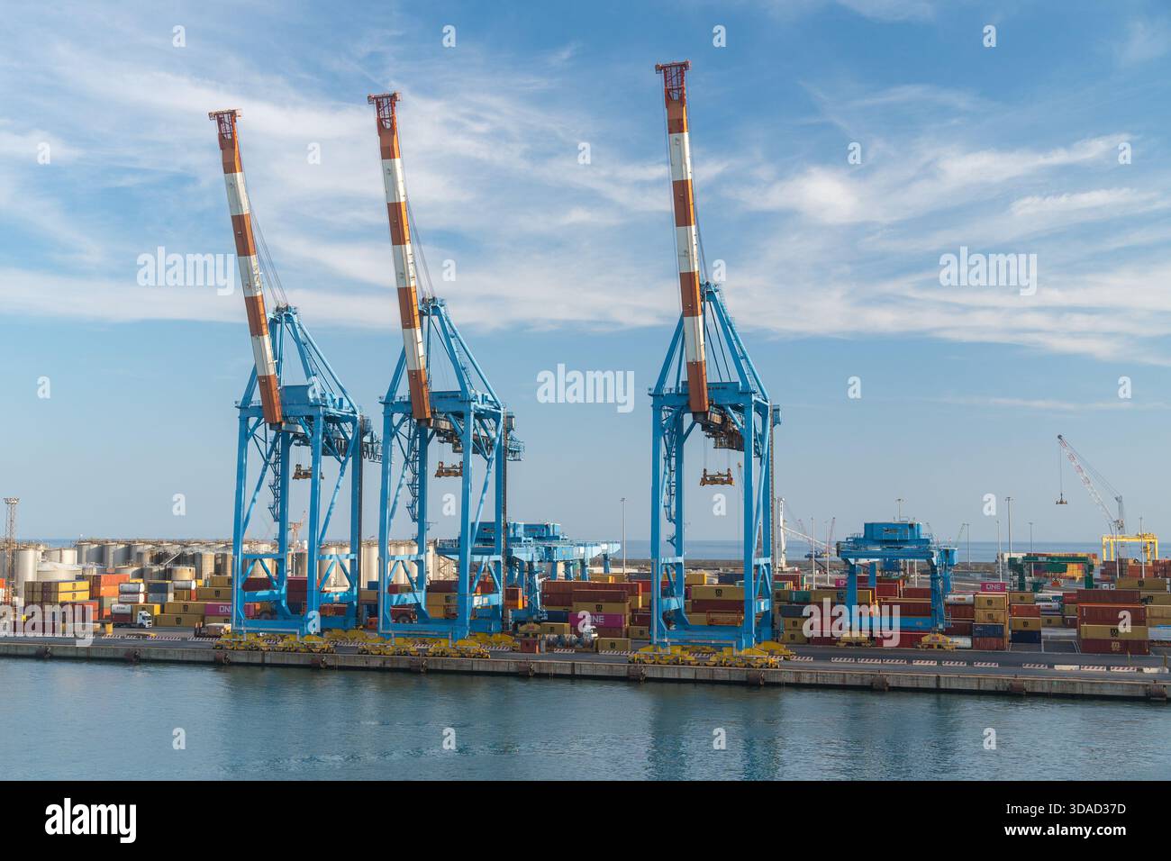 06.18.25, Genua, Italia, le gru portacontainer blu alte si trovano lungo la banchina del porto sotto un cielo luminoso. Macchinari industriali utilizzati per la movimentazione di carichi, con Foto Stock