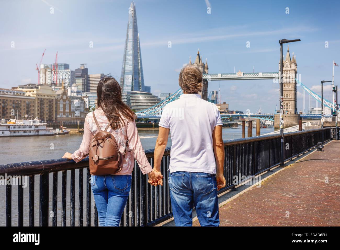 Un paio di passeggiate lungo la riva del Tamigi a Londra, Inghilterra, con vista sul Tower Bridge e lo skyline durante una giornata estiva Foto Stock