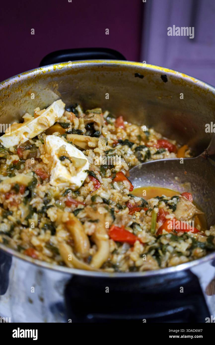 Primo piano di un tradizionale stufato greco fatto in casa con riso, spinaci, funghi, peperoni e formaggio feta in una pentola di acciaio inossidabile. Foto Stock