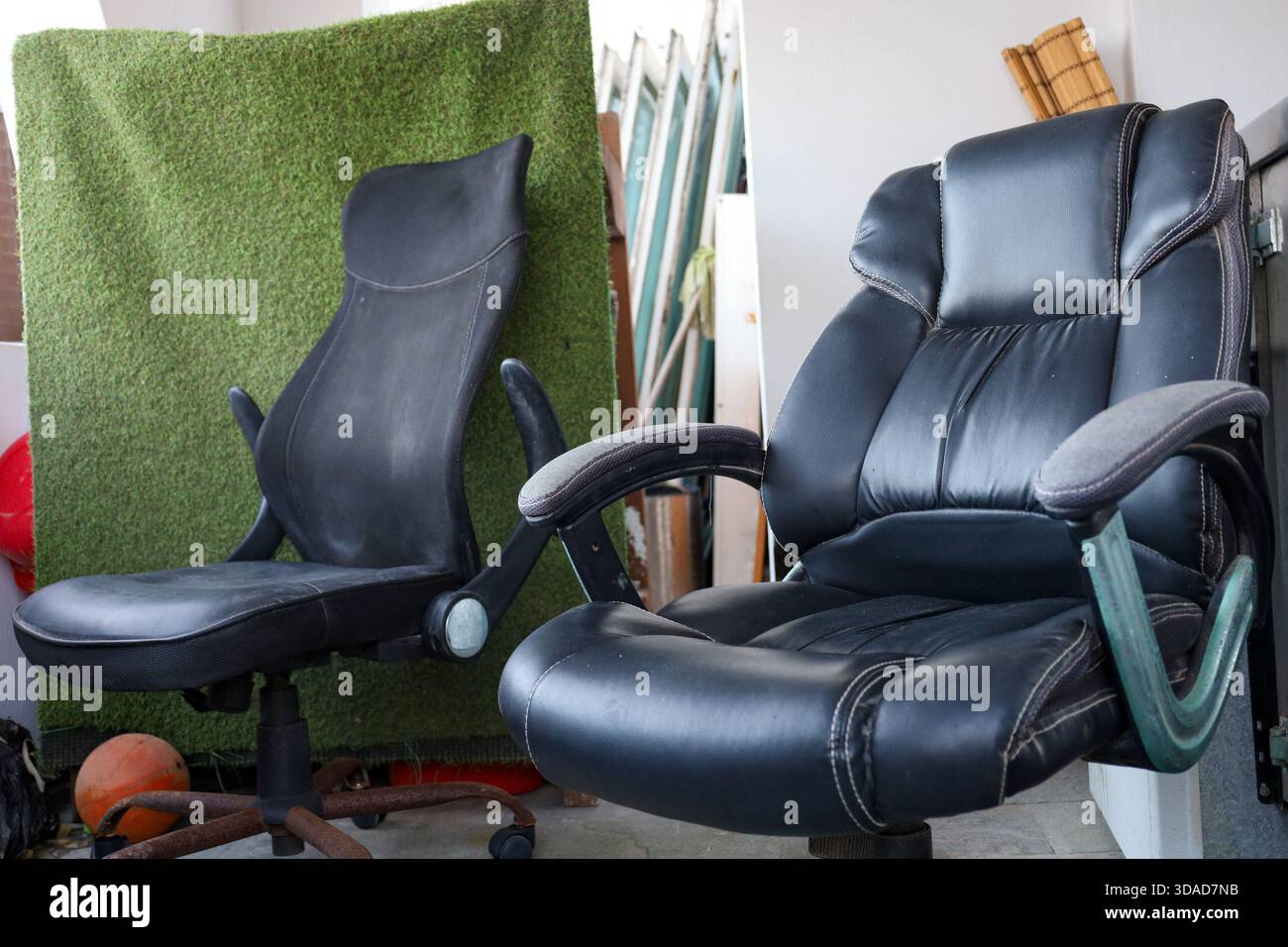 Due sedie da ufficio nere usate sono collocate in un ambiente ordinato, circondate da oggetti impilati e da uno sfondo testurizzato verde. Foto Stock