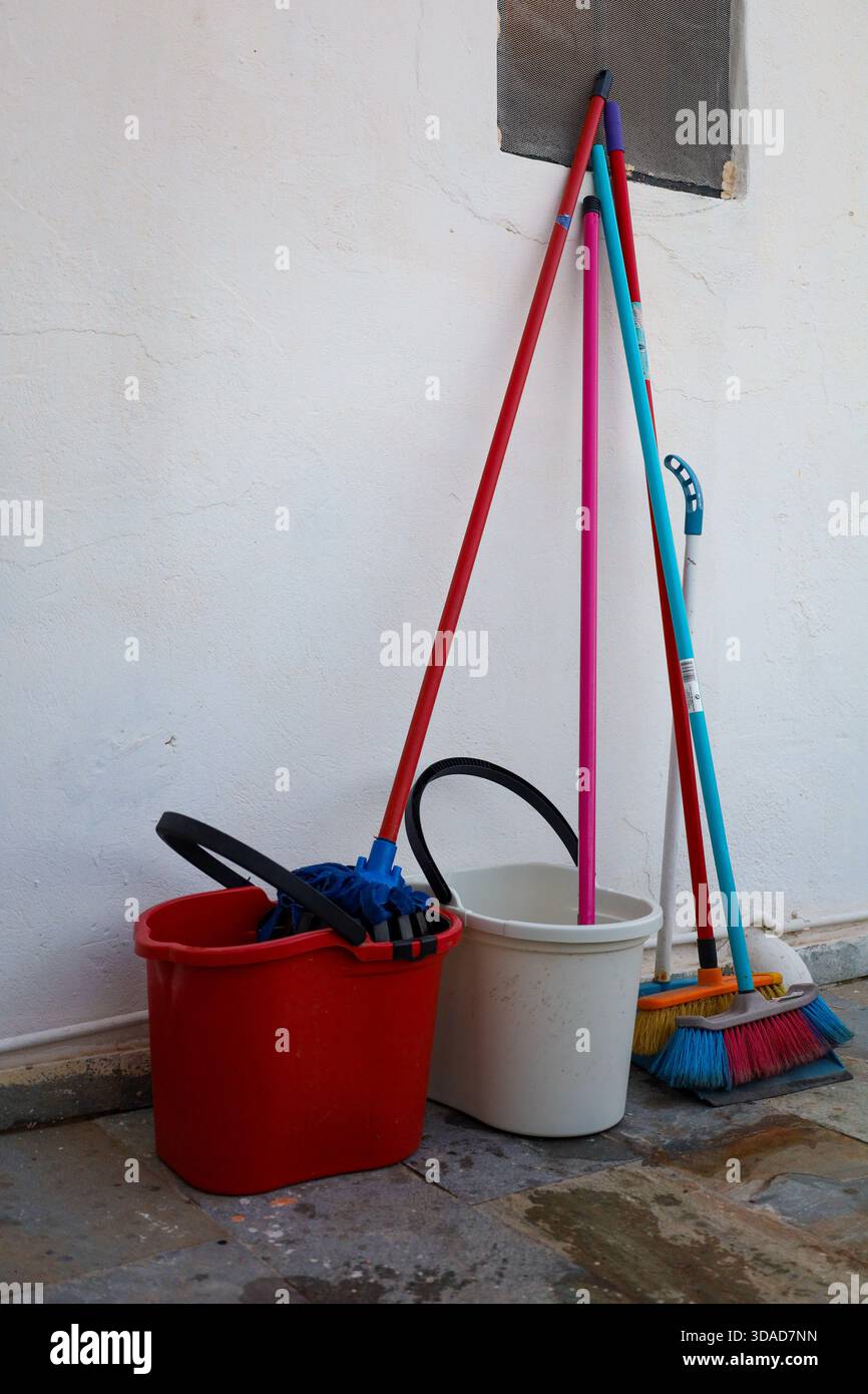 Un gruppo di utensili per la pulizia quotidiana si trova contro una parete bianca, tra cui spazzatrici, spazzoloni e secchi, ideali per lavori di sanificazione, lavori domestici e manutenzione Foto Stock