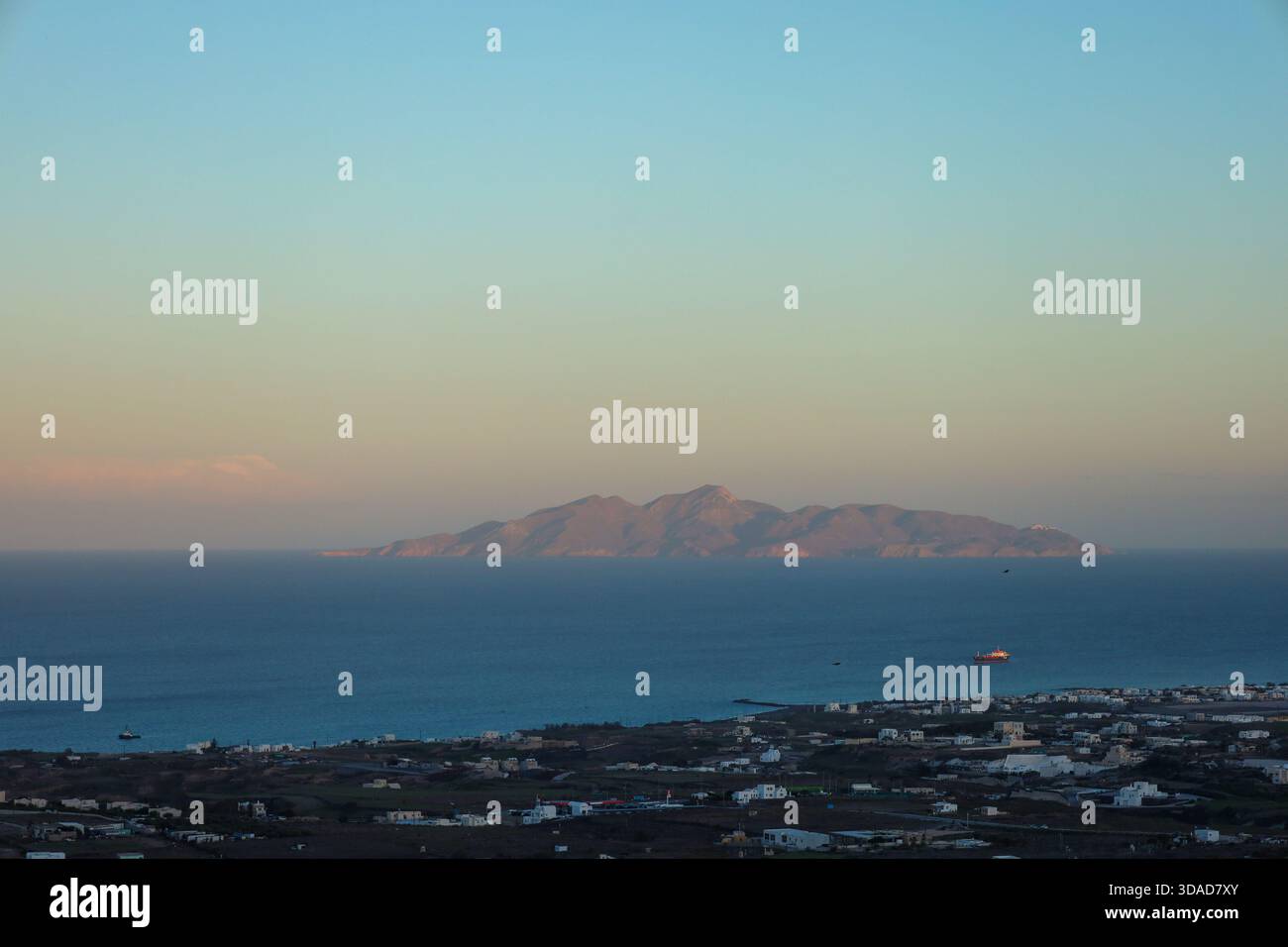 Vista distante dell'isola di Anafi da Santorini durante l'ora d'oro, con la calda luce del sole che esalta la silhouette rocciosa. Foto Stock