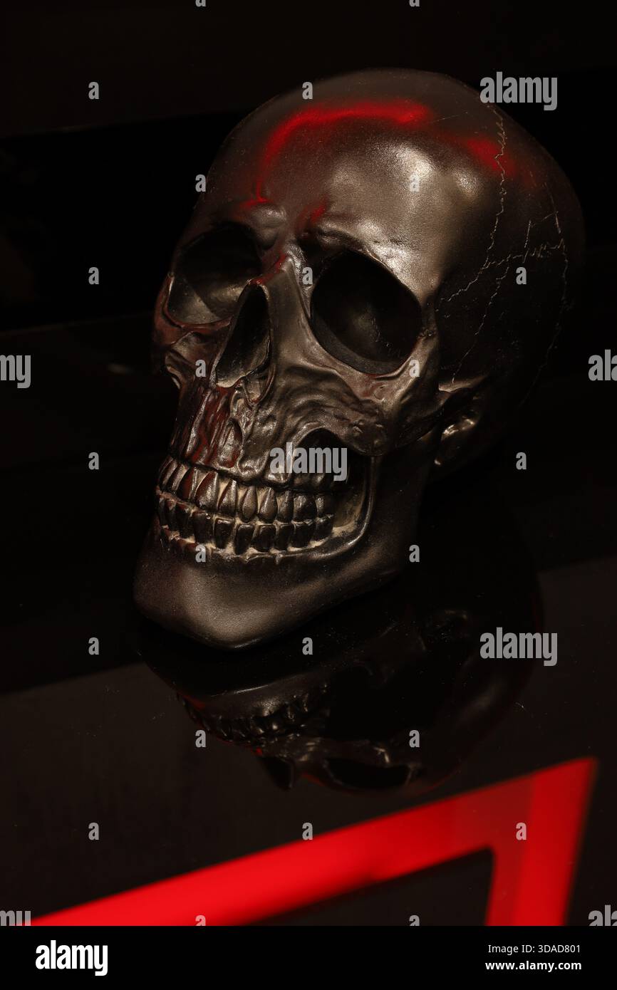 Un drammatico teschio nero illuminato da una vivace luce d'accento rossa, che crea una natura morta concettuale lunare perfetta per temi horror, Halloween e commerciali oscuri. Foto Stock