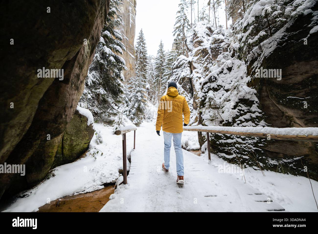 Uomo in abiti caldi che cammina attraverso il paesaggio innevato tra alte formazioni rocciose ad Adrspach in un freddo giorno d'inverno. La scena cattura i momenti più tranquilli all'aperto Foto Stock