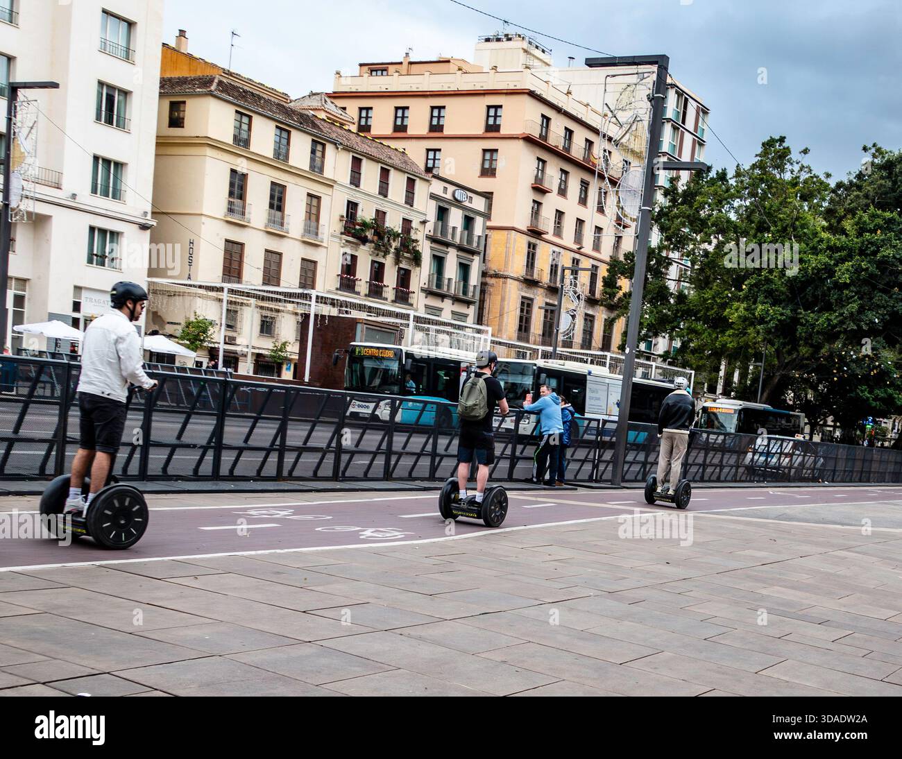 Tre persone che guidano scooter Segway autobilanciati. Malaga, Spagna, centro città, pista ciclabile rossa. Architettura storica, traffico di autobus, Foto Stock
