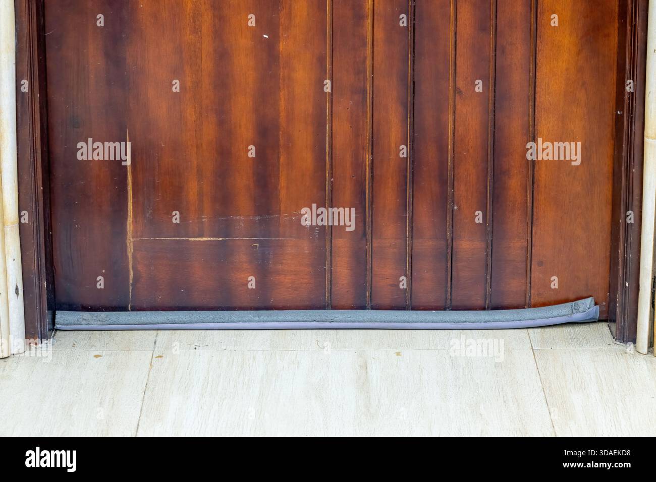 Primo piano di una porta in legno con un limitatore di sforzo (noto anche come serpente di trazione o protezione) per sigillare lo spazio sul fondo. Utilizzato per l'isolamento Foto Stock