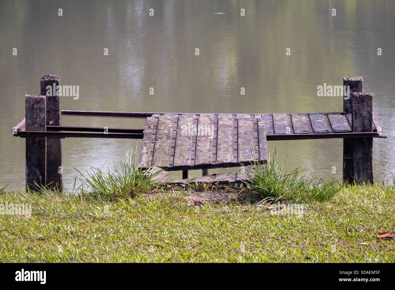 Una piccola banchina o panchina di legno intemprata si trova ai margini dell'acqua calma. Un ambiente rustico e tranquillo di un laghetto o di una sponda del fiume per la natura, il relax, Foto Stock